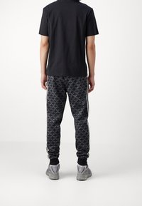 Černé tričko v kombinaci s černými vzorovanými tepláky s šedým motivem ptáka, bílými bočními pruhy a šedými sportovními botami.