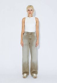 Volné džíny světle béžové barvy s vybledlým vzhledem, kombinované s bílým tílkem bez rukávů. Outfit doplňují béžové tenisky.