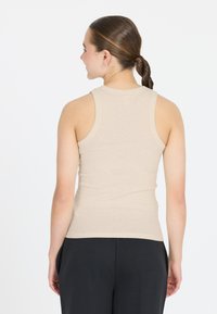 Beige, geripptes Tanktop mit hohem Ausschnitt und breiten Schulterträgern, von hinten gezeigt. Glatte Textur, figurbetonte Silhouette.