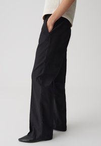 Pantalons larges noirs en mélange de coton, avec poches latérales, une texture lisse et une coupe décontractée. Porté avec un pull léger.