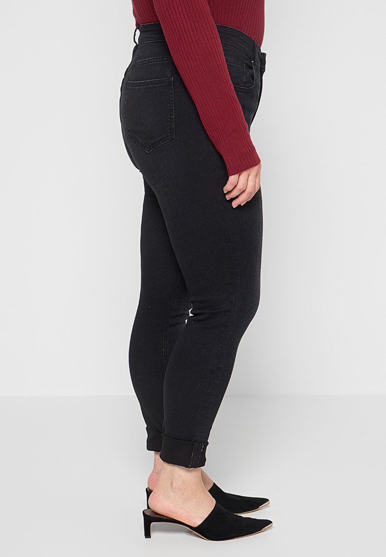 Schwarze Jeans aus Denim mit schmalem Schnitt, hoher Taille und umgeschlagenen Säumen, kombiniert mit einem burgunderfarbenen, gerippten Langarmoberteil und schwarzen offenen Mules.