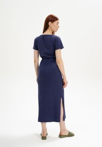 Dunkelblaues Kurzarmkleid mit Kordelzug in der Taille, Seitennaht und weichem Stoff. Getragen mit grünen Rutschsandalen.