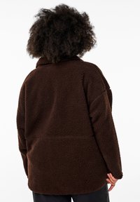 Braune Fleecejacke mit strukturierter Oberfläche, lockerer Passform und Kragen. Sie hat lange Ärmel und einen geraden Saum ohne sichtbare Verschlüsse.