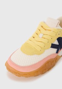 Sneaker featuring a textured white mesh upper with yellow and pink suede accents, yellow laces, and a translucent gum rubber sole.