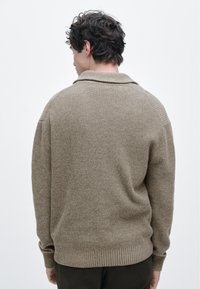 Pull beige tricoté avec une texture côtelée, doté d'un col châle et d'une coupe ample, présenté de dos sur un fond neutre.