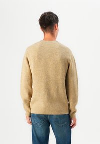 Pulôver de malha em bege com textura canelada, apresentando mangas longas e decote redondo, combinado com jeans de ganga azuis.
