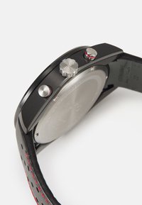 Black watch with a stainless steel case, rubberized crown and pushers, red accents, and a perforated black leather strap.