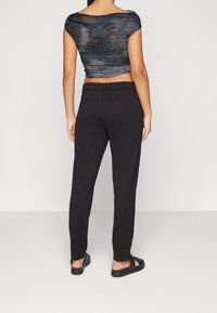 Svarta vida byxor med en slät textur och elastisk midja, i kombination med en mörk mönstrad kort topp med lager av tygdetaljer.