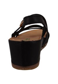 Sandales compensées en cuir noir avec un dos ouvert, un design de brides croisées et une semelle texturée de couleur brun clair. Rehaussées de subtils accents en or.