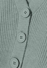 Cardigan à côtes vert clair avec quatre boutons assortis de forme ronde et quatre trous, présentant une texture légèrement chatoyante.
