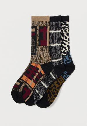 Three pairs of patterned socks: one in beige with geometric designs, one black and gray striped, and one black with light blue leopard spots.