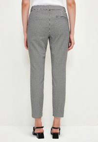 Pantalon à motif vichy noir et blanc, coupe slim, avec une poche arrière et une texture de tissu lisse. Porté avec des chaussures noires à talons blocs.