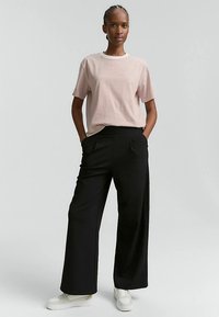 Randig rosa och vit T-shirt med korta ärmar kombinerad med svarta byxor med vida ben och vita sneakers, som visar en avslappnad passform och mjuk textur.