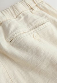 Makroaufnahme von cremefarbenen Stoffhosen mit einer Gesäßtasche mit Knopfverschluss und elastischem Bund.