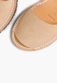 Zamszowe buty wsuwane, w kolorze jasnobeżowym, z okrągłym noskiem, kontrastowym białym szwem oraz brązową gumową podeszwą; widoczne detale szwów na krawędziach.