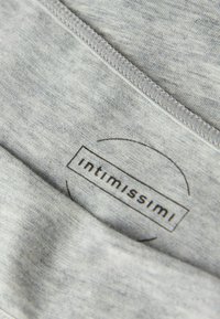 Szary materiał o miękkiej fakturze, z wyraźną czarną metką z napisem "intimissimi" otoczoną okrągłym wzorem i subtelnymi przeszyciami.