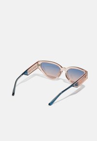 Occhiali da sole cat-eye con montatura rosa traslucida e lenti blu sfumate. Le aste presentano un accento blu e il marchio "GUESS".