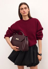 Bordowa skórzana torebka o strukturalnym designie, z hardwarem w kolorze złota oraz uchwytem na górze. W zestawie z bordowym swetrem i czarną spódnicą.