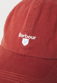 Punane pesapalli müts valge "Barbour" tekstiga ja väike valge ja sinine kilp tikandiga esipaneelil.
