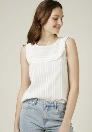 Haut sans manches blanc avec un col froncé, présentant des rayures horizontales et des détails fins. Associé à un jean en denim bleu clair.