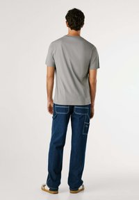 Tricou gri cu mânecă scurtă, asociat cu pantaloni din denim albastru, care au multiple buzunare și cusături în contrast. Pantofii plat completează ținuta.