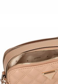 Borsa a tracolla beige trapuntata con doppie cerniere dorate e logo Guess sul davanti, che mostra l'interno foderato in tessuto beige.