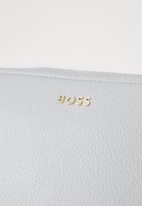 Portafoglio in pelle grigia con superficie testurizzata, caratterizzato da un piccolo logo dorato "BOSS". Cuciture visibili lungo il bordo.