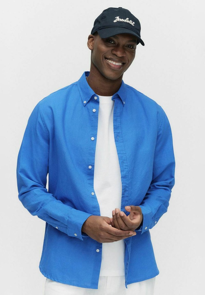 Blauwe button-up blouse van lichtgewicht stof, met een kraag, lange mouwen en een ontspannen pasvorm. Gecombineerd met een wit T-shirt eronder.