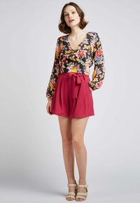 Haut à manches longues floral avec un décolleté en V plongeant, associé à des shorts bordeaux taille haute mettant en avant un détail de nœud à l'avant et un tissu texturé.