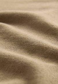 Weiches, hellbraunes Gewebe mit glatter Textur, das eine feingestrickte Konstruktion aufweist und subtile Variationen in der Oberflächenstruktur zeigt.