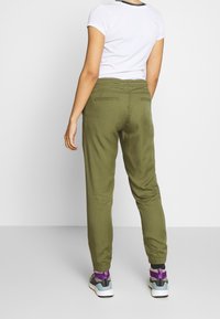 Kahakjoggers med elastiska muddar och två bakfickor, kombinerade med en vit kortärmad skjorta och sportskor.