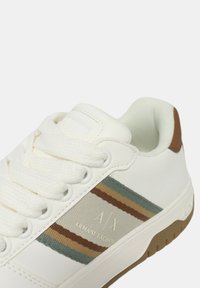 Sneaker bianco con tomaia in pelle testurizzata, lacci piatti e suola in gomma. Presenta strisce multicolori (beige, marrone, teal) e dettagli del logo.