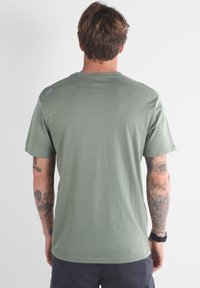T-shirt vert olive en coton doux, avec des manches courtes, un col rond et un petit logo sur l'épaule gauche.