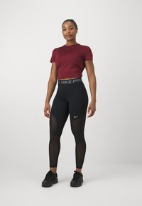 Burgundi värvi sobiv t-särk ja mustad Nike Pro retuusid, millel on võrgusilma paneelid. Retuusidel on vöö kohal logo ja need on sujuva tekstuuriga.