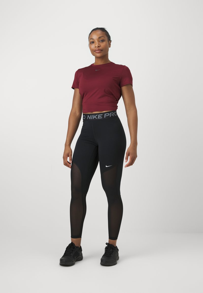 T-shirt ajusté bordeaux et leggings noirs Nike Pro avec des panneaux en maille. Les leggings ont un logo sur la taille et une texture lisse et soyeuse.
