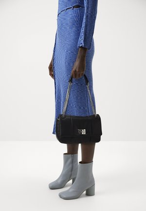 Person wearing a blue ribbed midi dress and light gray ankle boots, holding a black handbag with silver chain straps.