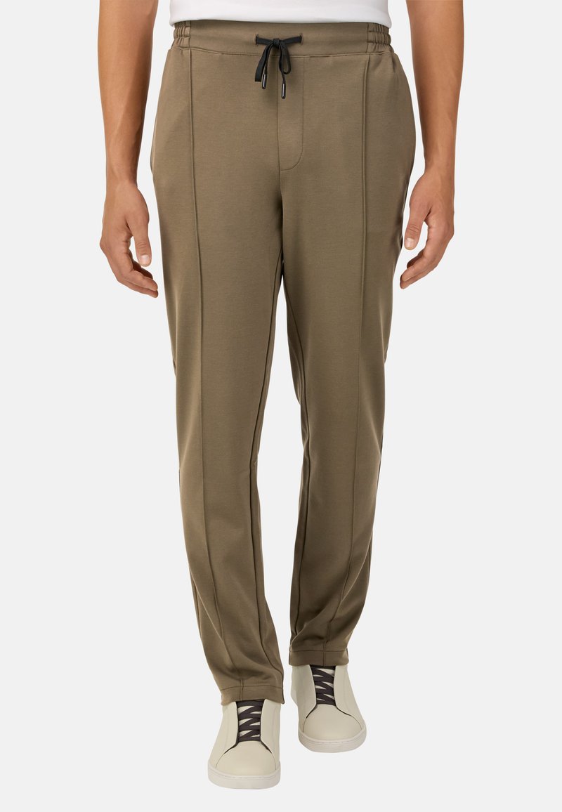 Alyvuogių žalios spalvos sportinės kelnės, pagamintos iš švelnaus audinio, turinčios elastingą juosmenį su raišteliu, šonines kišenes ir subtilius siūlus.