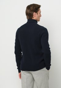 Marineblaue gerippte Strickrollkragensweater mit langen Ärmeln, mit einem figurschmeichelnden Design und einfarbiger Textur, kombiniert mit hellgrauen Hosen.