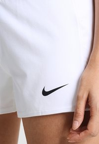 Vita idrottsshorts i slät tyg har en svart Nike-logotyp på nedre vänstra sida. Shortsen har en enkel, funktionell design.