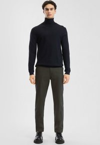 Maglione a collo alto blu navy, design aderente, abbinato a pantaloni verde oliva. Scarpe nere stringate con suola spessa completano il look.