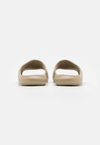 Beige slip-on szandálok nyitott háttal és oldalakkal, texturált felsőrésszel és sima, kerek talppal a kényelem érdekében.