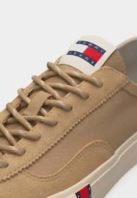 Μπεζ αθλητικό παπούτσι με υφασμάτινη υφή και πάνελ από σουέντ, μπεζ κορδόνια και λογότυπο Tommy Jeans στη γλώσσα και στο πλάι της σόλας.