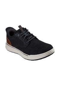 Zapatilla de punto negra con un cuello acolchado, cordones grises y un acento de cuero marrón. Presenta una suela ligera y flexible con una entresuela blanca.