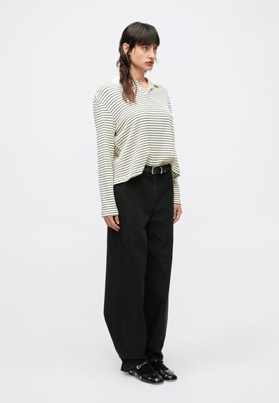 Pruhovaná košeľa s dlhým rukávom v krémovej a čiernej farbe, voľný strih. Kombinovaná s čiernymi širokými nohavicami s vysokým pásom a čiernymi slip-on topánkami.
