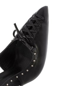 Scarpa in pelle nera con punta affusolata, caratterizzata da lacci incrociati e borchie argentate lungo il lato. Superficie interna testurizzata.