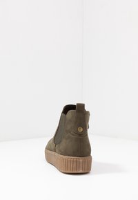 Gröna mocka ankstövlar med elastiska sidor, rund tå och texturerad gummisula. Har en dekorativ mässingsknapp på klacken.