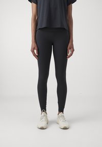 Czarne prążkowane legginsy z wysokim stanem, zestawione z luźną ciemnoszarym topem. Osoba ma na sobie jasne buty sportowe.