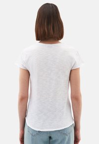 Witte t-shirt met korte mouwen en een licht gestructureerde afwerking, ronde halslijn en afgeronde zoom, gedragen met lichtblauwe jeans.