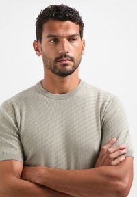 Lichtgroene gebreide trui met korte mouwen en een ronde halslijn. Bevat een ruitpatroon en ribgebreide manchetten.