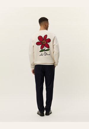 Cream sweatshirt featuring a large red flower graphic on the back, with green leaves and black outline. Text reads "Les Deux." Worn with dark pants.